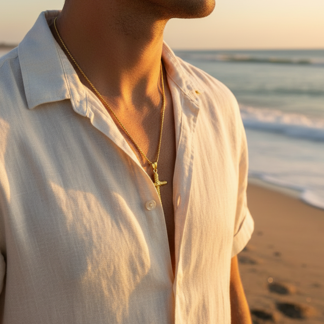 Man wearing a light-colored shirt and necklace on a beach at sunset