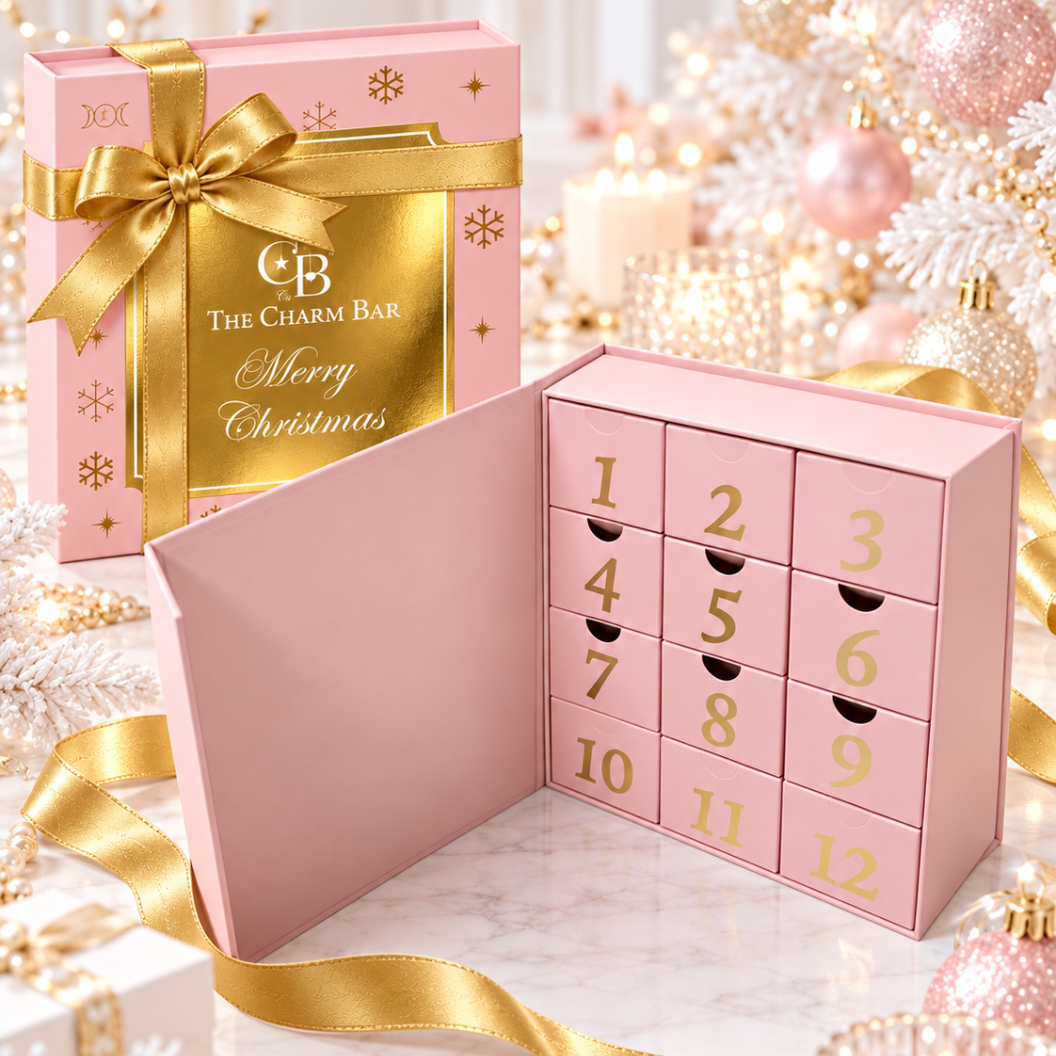 The Charm Bar Company Heirloom Advent Calendar featuring an open pink jewelry gift box with 12 numbered surprise drawers, gold ribbon, and festive Christmas decorations.