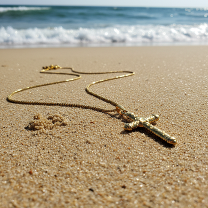 Gold necklace with a cross pendant on a sandy beach with ocean waves in the background
