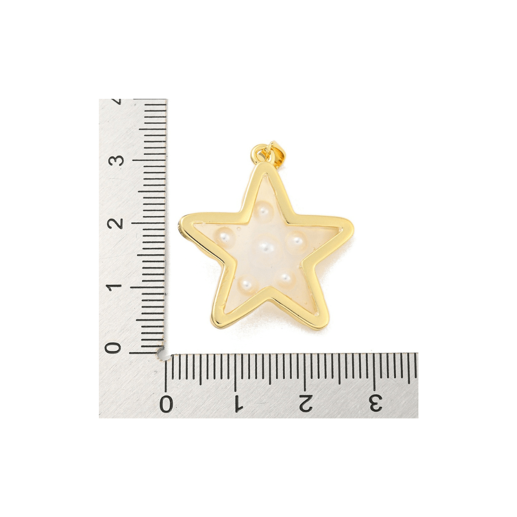 Gold star-shaped pendant with a white center next to a ruler on a white background