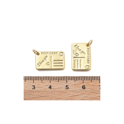 Front and side view of the Gold Post Card Charm compared to a ruler