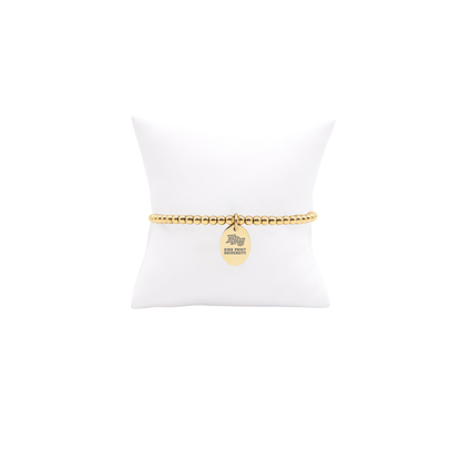 High Point University gold beaded bracelet with small oval charm with high point university text and hpu logo displayed on white pillow front view
