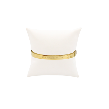 Kappa Delta gold bangle bracelet with full sorority name on white pillow front view