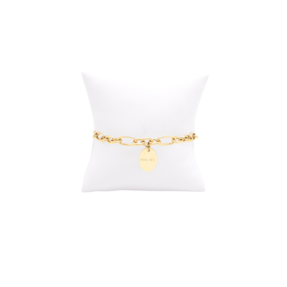 Phi Mu gold link Keepsake bracelet with small oval charm with full sorority name on white pillow front view
