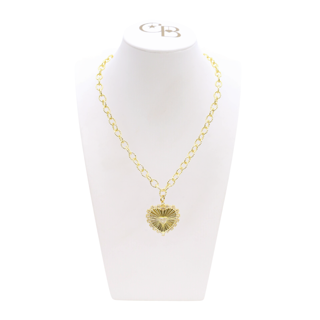 Gold necklace with a heart-shaped pendant on a white stand with a visible brand logo.