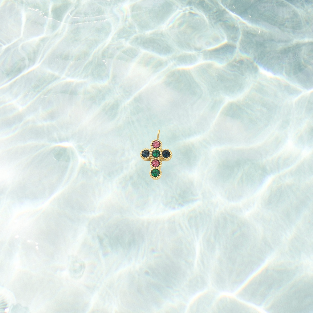Gold cross pendant with colored gemstones on a light blue textured surface