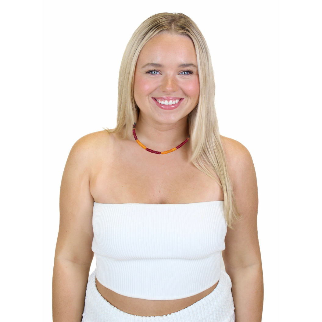 Woman wearing a white strapless top and skirt with a red necklace on a white background