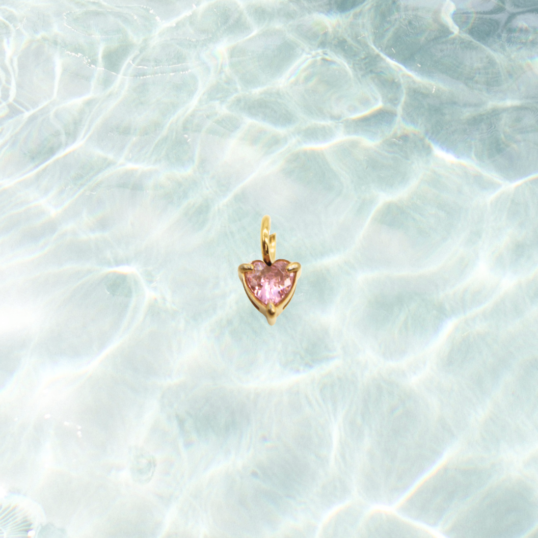Heart-shaped pink gemstone pendant on a light blue textured background