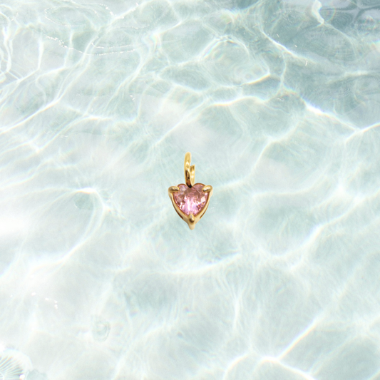 Heart-shaped pink gemstone pendant on a light blue textured background