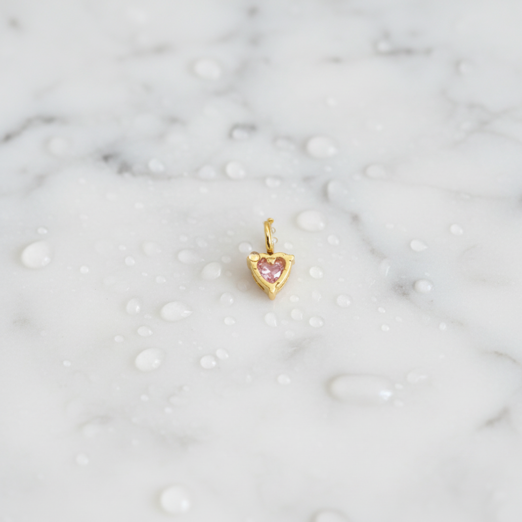 Gold heart-shaped pendant with a pink gemstone on a marble background