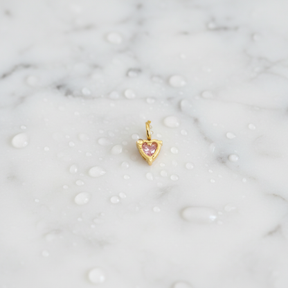 Gold heart-shaped pendant with a pink gemstone on a marble background