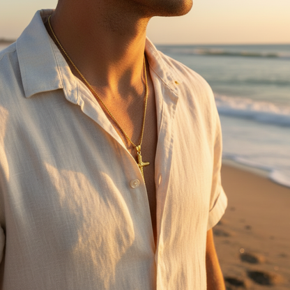 Man wearing a light-colored shirt and necklace on a beach at sunset