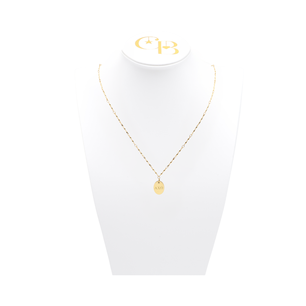 Alpha Chi Omega gold twist necklace with small oval charm with horizontal greek letters on white pillow front view.
