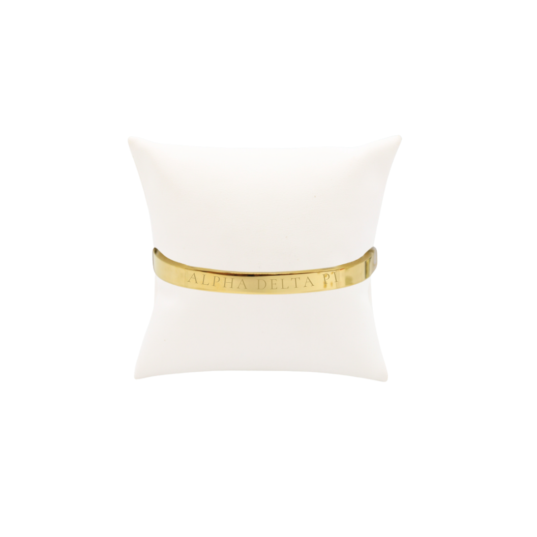Alpha Delta Pi gold bangle bracelet with full sorority name on white pillow front view.