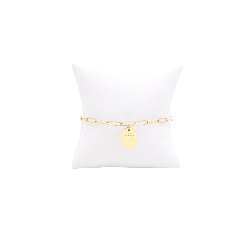 Alpha Delta Pi gold link storyline bracelet with small oval charm with full sorority name on white pillow front view.