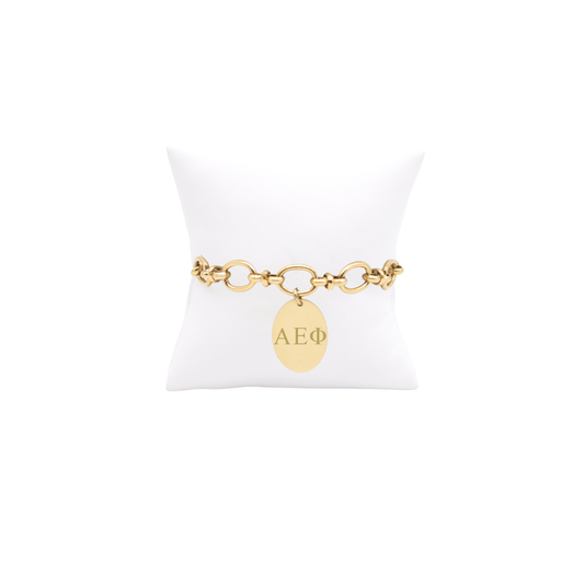 Alpha Epsilon Phi gold large link evermore bracelet with large oval charm displayed on white pillow front view with horizontal greek letters