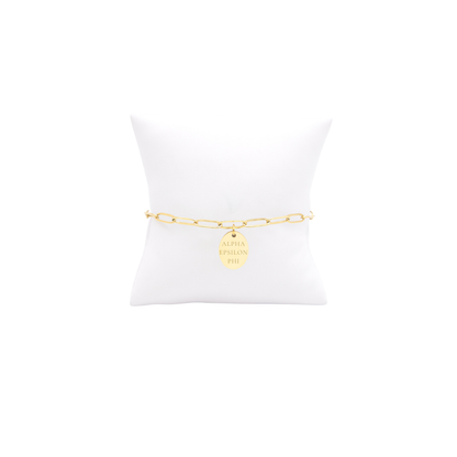 Alpha Epsilon Phi gold large link keepsake bracelet with small oval charm displayed on white pillow front view with vertical/stacked greek letters