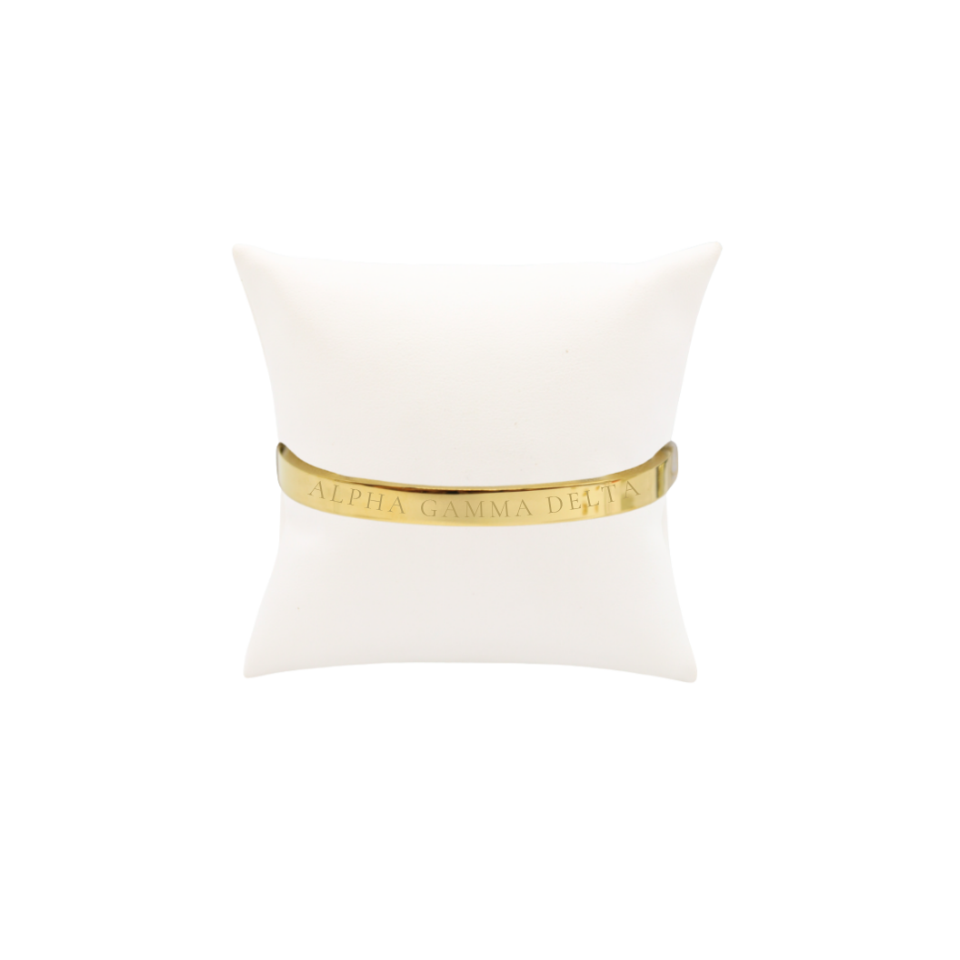Alpha Gamma Delta gold bangle bracelet displayed on white pillow front with full sorority name