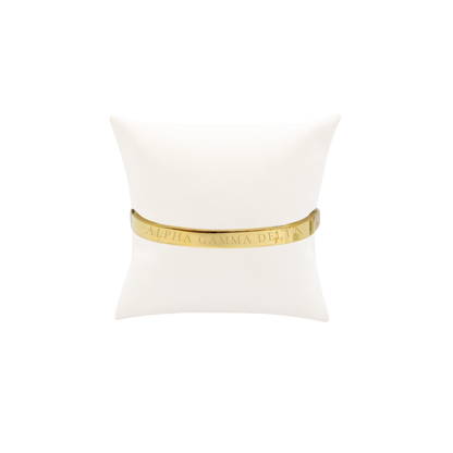 Alpha Gamma Delta gold bangle bracelet displayed on white pillow front with full sorority name