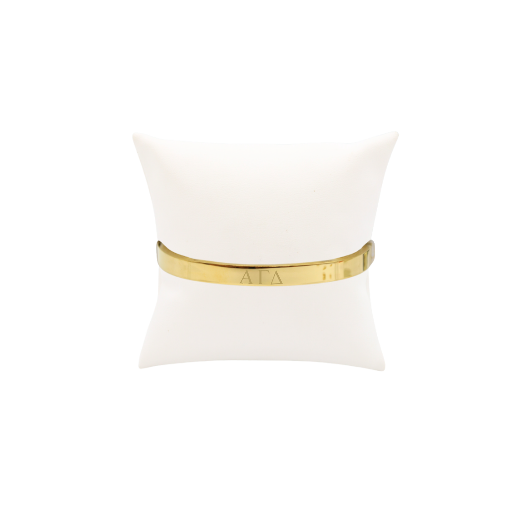 Alpha Gamma Delta gold bangle bracelet displayed on white pillow front with horizontal greek letters