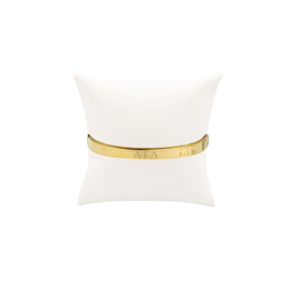 Alpha Gamma Delta gold bangle bracelet displayed on white pillow front with horizontal greek letters