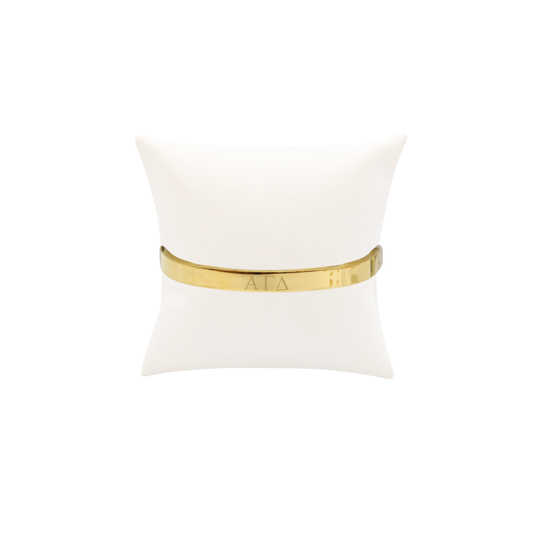 Alpha Gamma Delta gold bangle bracelet displayed on white pillow front with horizontal greek letters