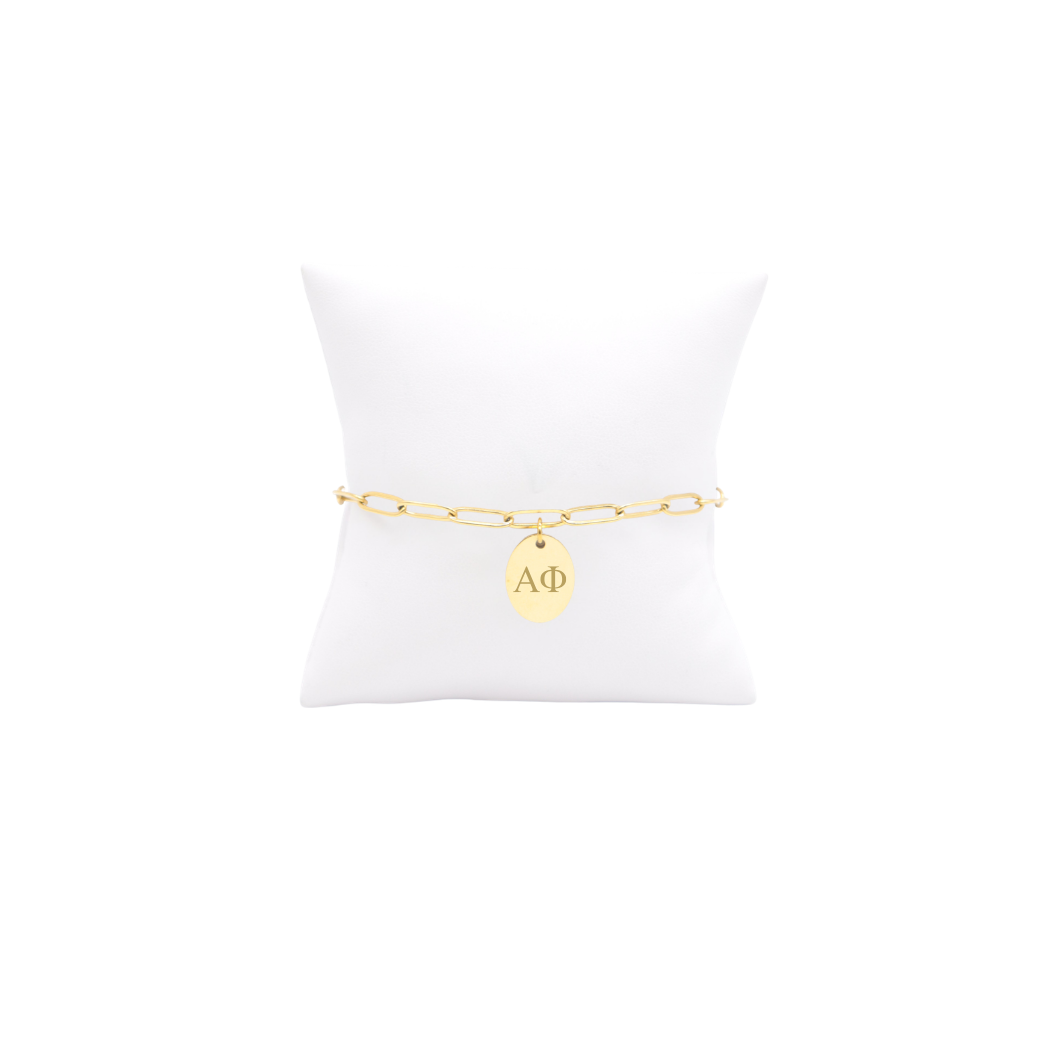 Alpha Phi gold link storyline bracelet with small oval charm with horizontal greek letters on white pillow front view