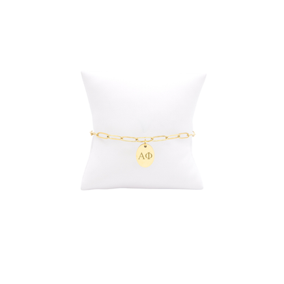 Alpha Phi gold link storyline bracelet with small oval charm with horizontal greek letters on white pillow front view