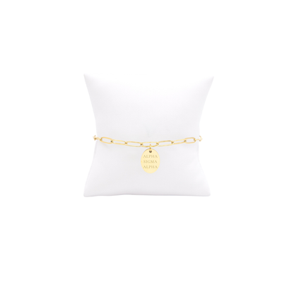 Alpha Sigma Alpha gold link storyline bracelet with small oval charm displayed on white pillow front view with full sorority name