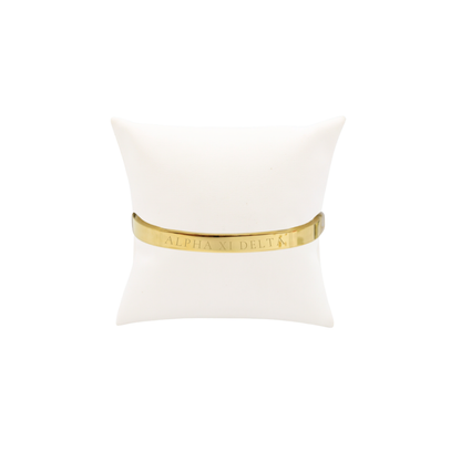 Alpha XI Delta gold bangle bracelet displayed on white pillow front view with full sorority name