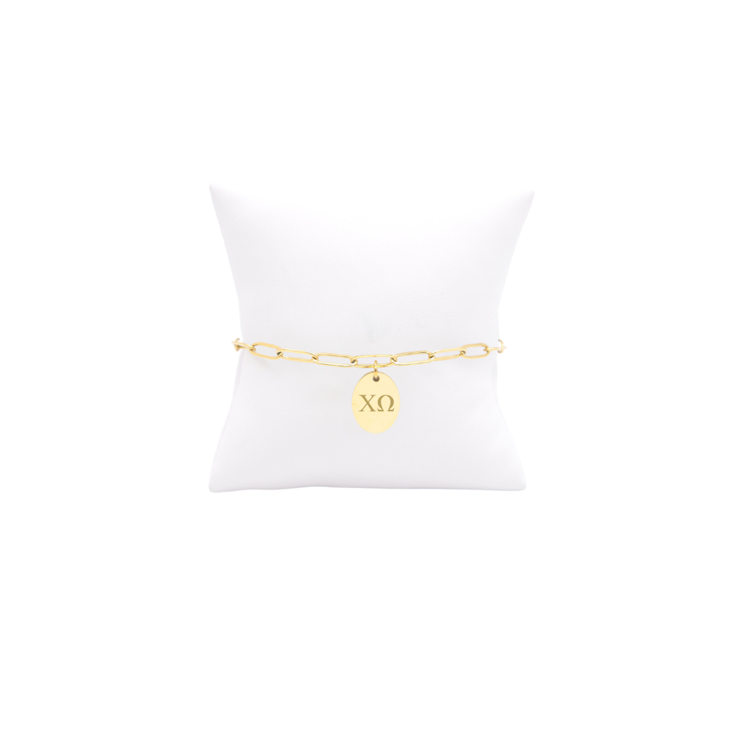 Chi Omega gold link storyline bracelet with small oval charm with horizontal greek letters on white pillow front view
