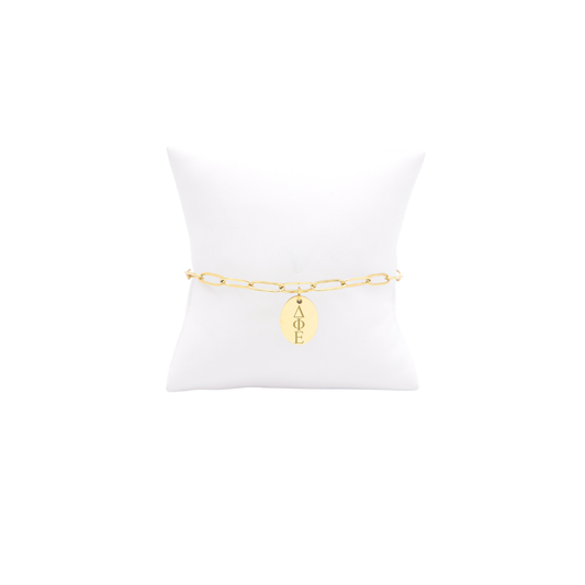 Delta Phi Epsilon gold link storyline bracelet with small oval charm displayed on white pillow front view horizontal greek letters