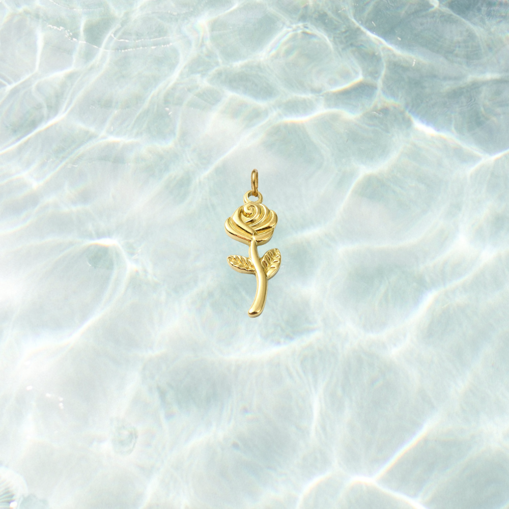 Gold rose charm with detailed petals, textured leaves, and a polished stem on a shimmering water background.