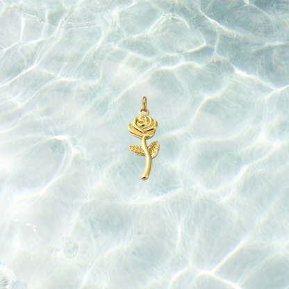 Gold rose charm with detailed petals, textured leaves, and a polished stem on a shimmering water background.