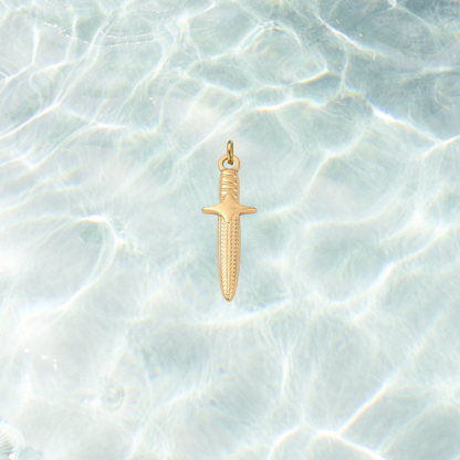 Gold dagger charm featuring engraved blade details and a polished finish on a shimmering water background.