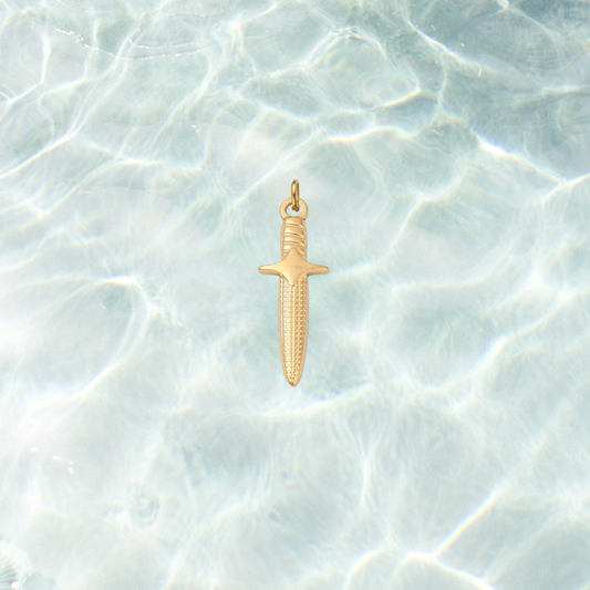 Gold dagger charm featuring engraved blade details and a polished finish on a shimmering water background.