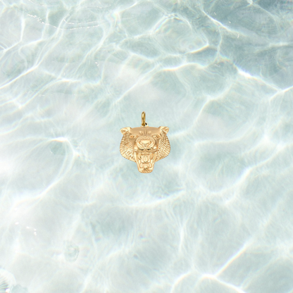 Gold fierce tiger head charm with detailed engraved features on a shimmering water background.