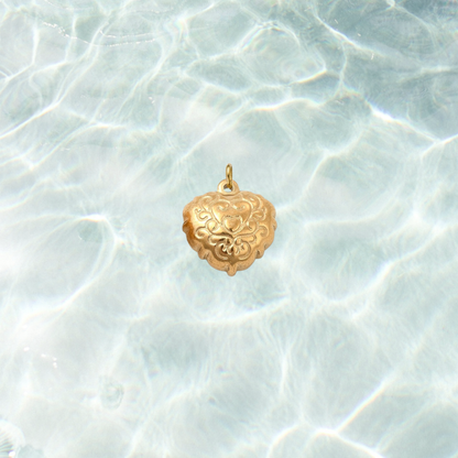 Gold filigree heart charm with an ornate engraved scrollwork design on a shimmering water background.