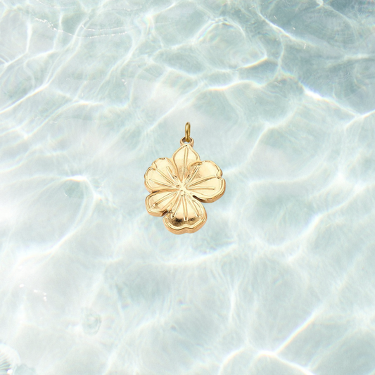 Gold hibiscus flower charm with engraved petal details and a polished finish on a shimmering water background.