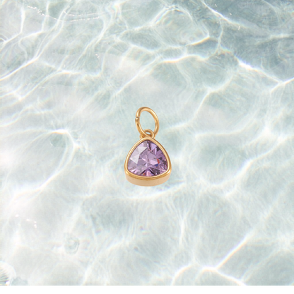 Gold triangular charm featuring a faceted lavender purple gemstone on a shimmering water background.