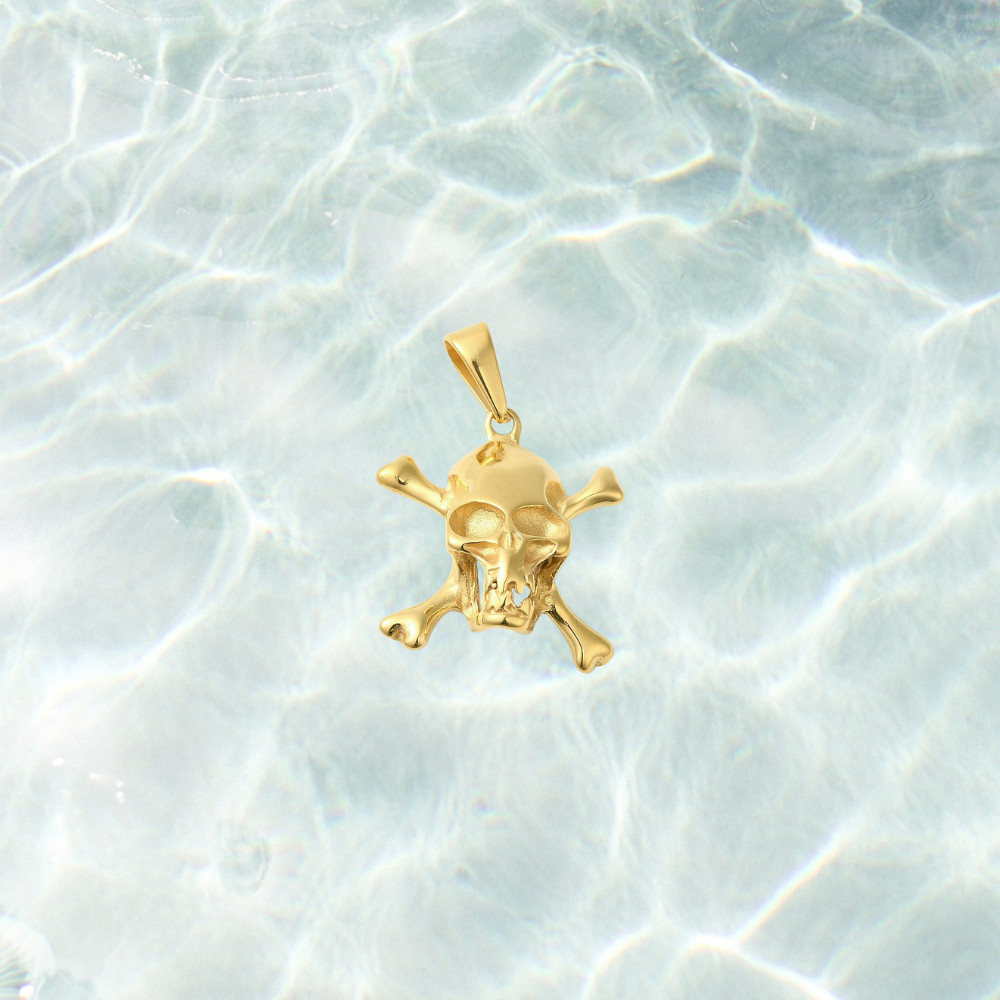Gold Pirate Skull Charm featuring a detailed skull and crossbones design with a polished gold finish, displayed on a light blue water-inspired background. Perfect for charm necklaces, bracelets, and pirate-inspired jewelry.