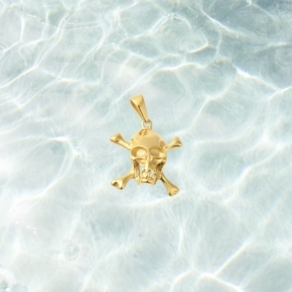 Gold Pirate Skull Charm featuring a detailed skull and crossbones design with a polished gold finish, displayed on a light blue water-inspired background. Perfect for charm necklaces, bracelets, and pirate-inspired jewelry.