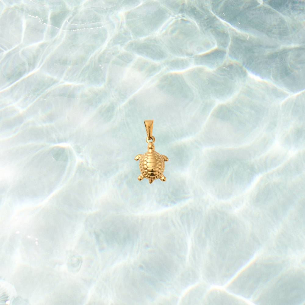 Gold sea turtle charm with a textured shell and polished finish on a shimmering water background.