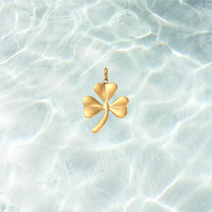 Gold shamrock charm featuring a polished three-leaf clover design on a shimmering water background.