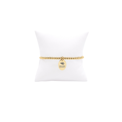 High Point University gold beaded bracelet with small oval charm with high point university text and panther logo displayed on white pillow front view
