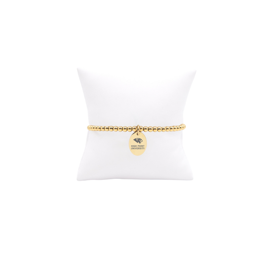 High Point University gold beaded bracelet with small oval charm with high point university text and panther logo displayed on white pillow front view
