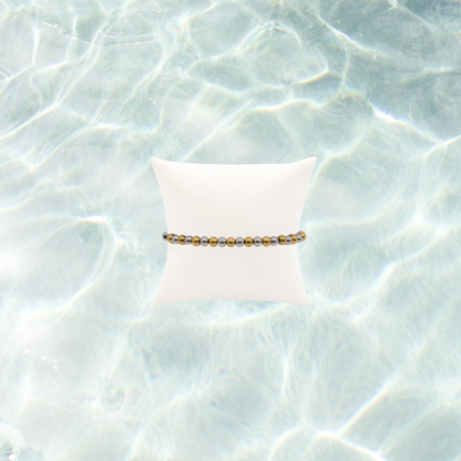 Mixed metal beaded stretch bracelet featuring alternating gold and silver stainless steel beads displayed on a white bracelet pillow on a waterproof background
