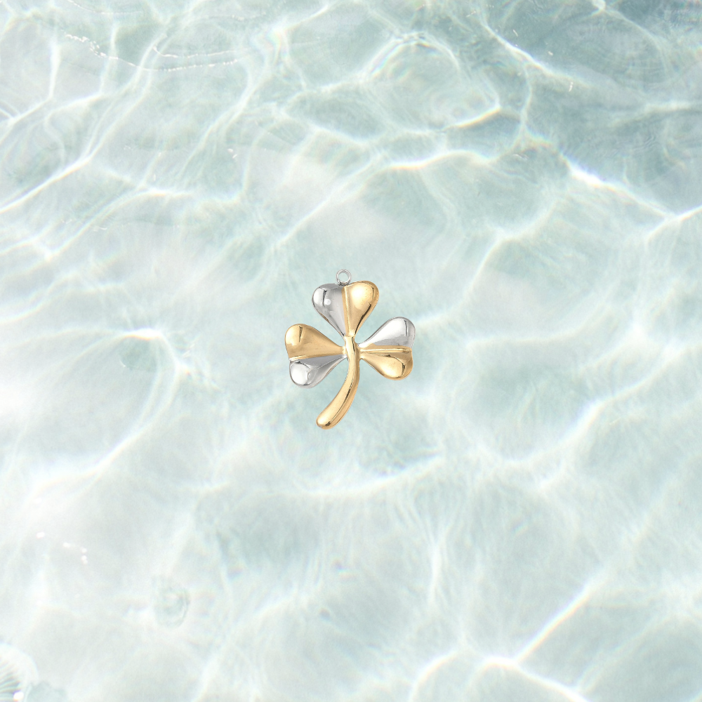 Mixed metal shamrock charm featuring alternating gold and silver leaves displayed on a shimmering light blue water background.