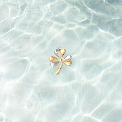 Mixed metal shamrock charm featuring alternating gold and silver leaves displayed on a shimmering light blue water background.