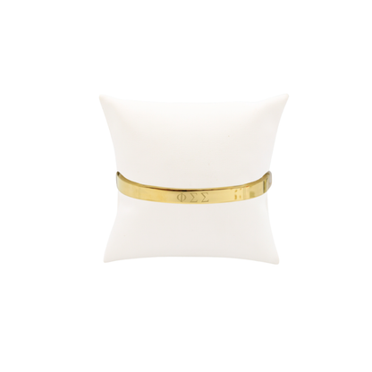 Phi Sigma Sigma gold bangle bracelet displayed on white pillow front view with horizontal greek letters